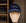 A navy Saint Talisman Cord Cap is showcased on a beige mannequin head, set against shelves lined with folded clothes. This cap features classic white embroidery and evokes the timeless charm of a traditional British hat through its elegant design.