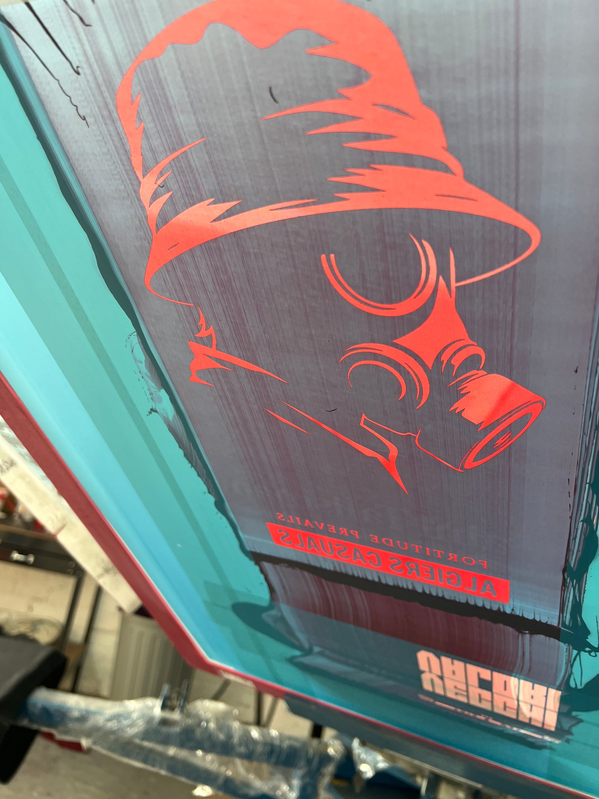 The SAINT TALISMAN x ALGIERS CASUALS screen printing frame features a red stencil of a person in a bucket hat and gas mask, with mirrored text “ALDER’S CASUALS” and “FORTITUDE RIVALS” beneath, evoking football culture.