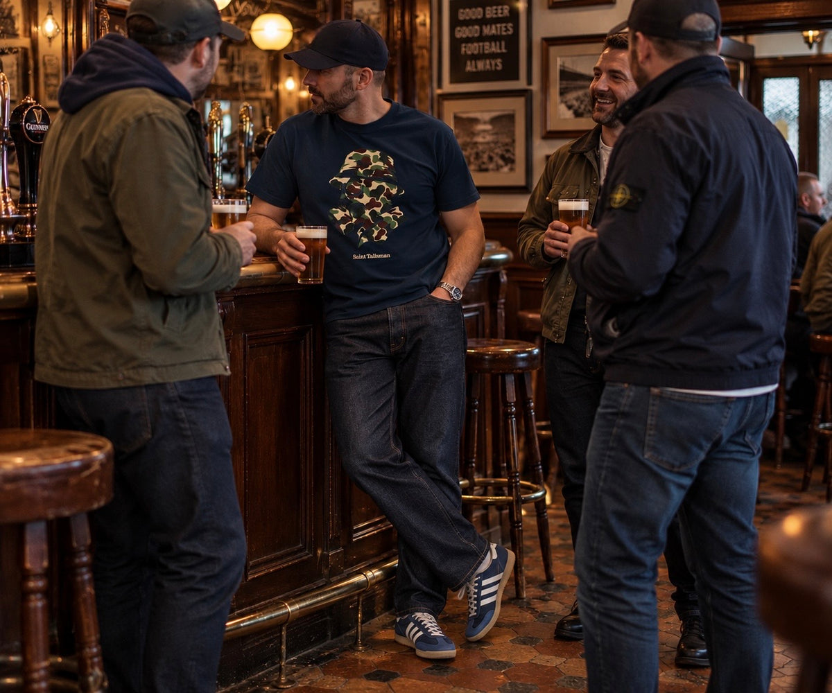 Four men stand at a pub bar, one wearing a navy CAMO GAS MASK T-SHIRT featuring a camouflage gas mask graphic.