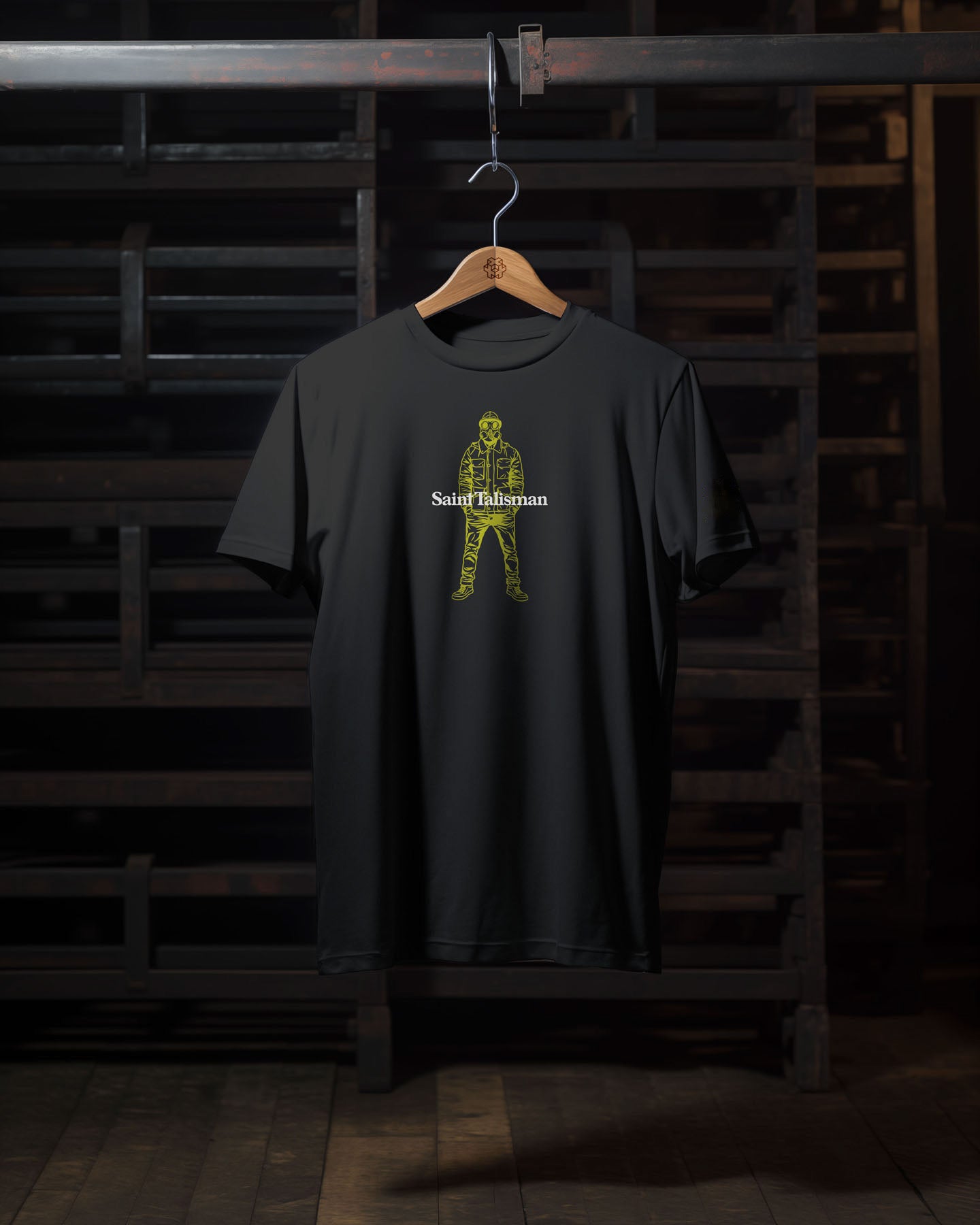 The Urban Gasman T-Shirt - Black & Yellow, crafted from organic cotton, features a medium fit with a yellow patterned person outline and "Saint Talisman" in white on the chest, displayed on a wooden hanger in a dim room.