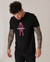 A man with curly hair and tattooed arms looks down while wearing a medium fit Alpine Gasman T-Shirt in black, made from organic cotton, featuring a pink graphic and "Saint Talisman" text on the front.